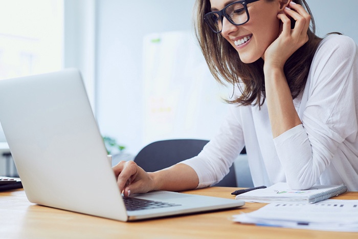 Woman with glasses smiling while looking at her laptop