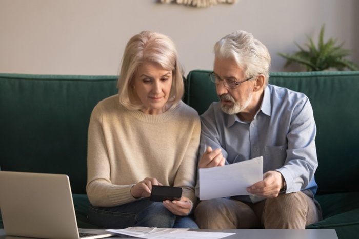 Older man and woman sitting on couch looking at papers and laptop