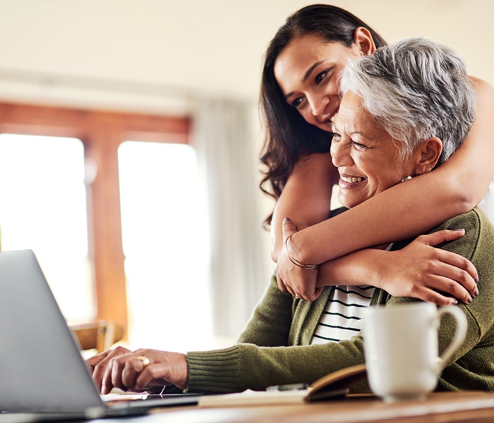 Student hugging grandmother who's looking at her laptop