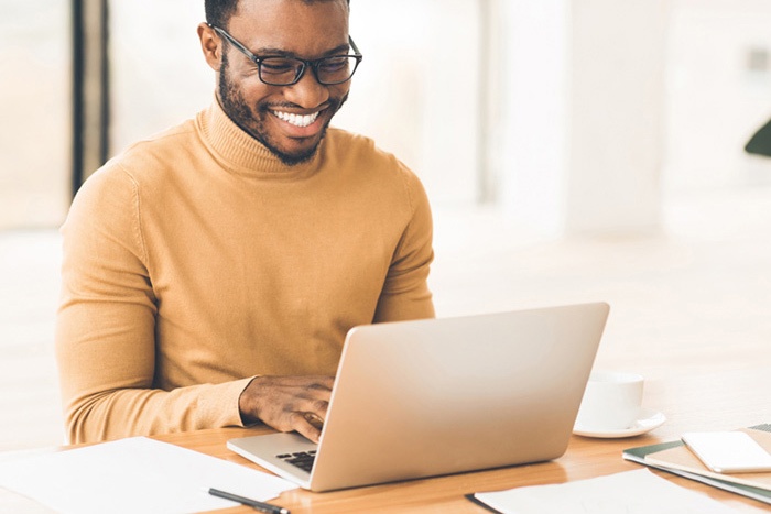 Man with glasses typing on laptop while in an office setting