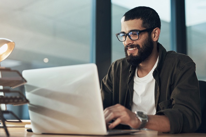 Man with glasses typing on laptop while in an office setting