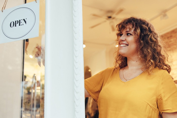 Woman at front of retail business looking at the open sign