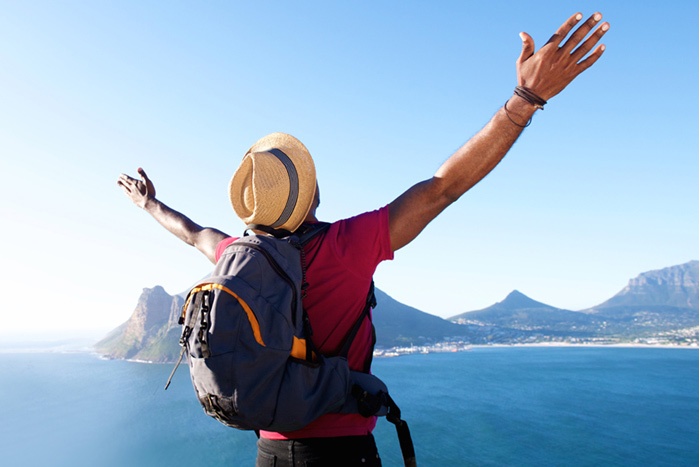 Traveler with backpack and arms in the air looking at an island and the open water