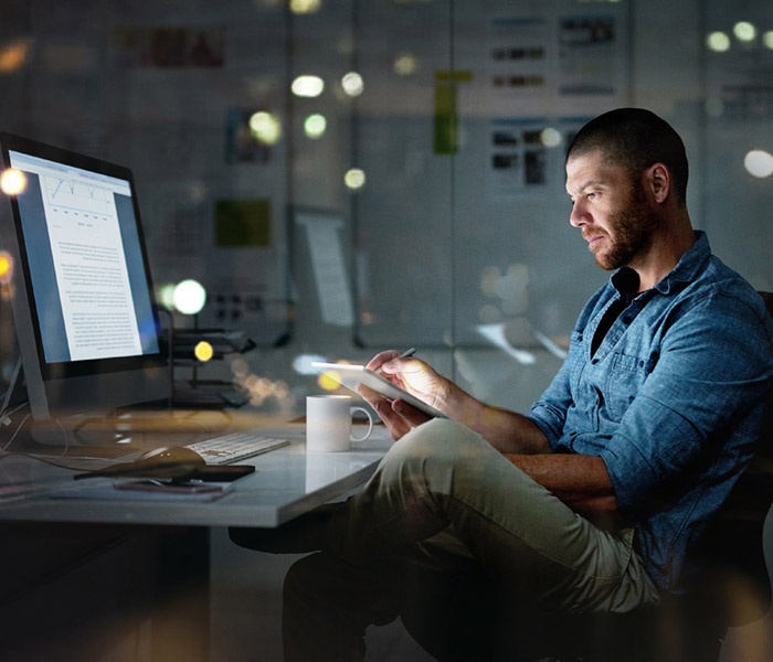 Man in office setting sitting at his desk with computer while writing notes